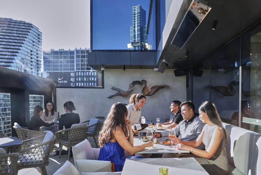 A group of people enjoying drinks at a rooftop bar, with city buildings in the background.