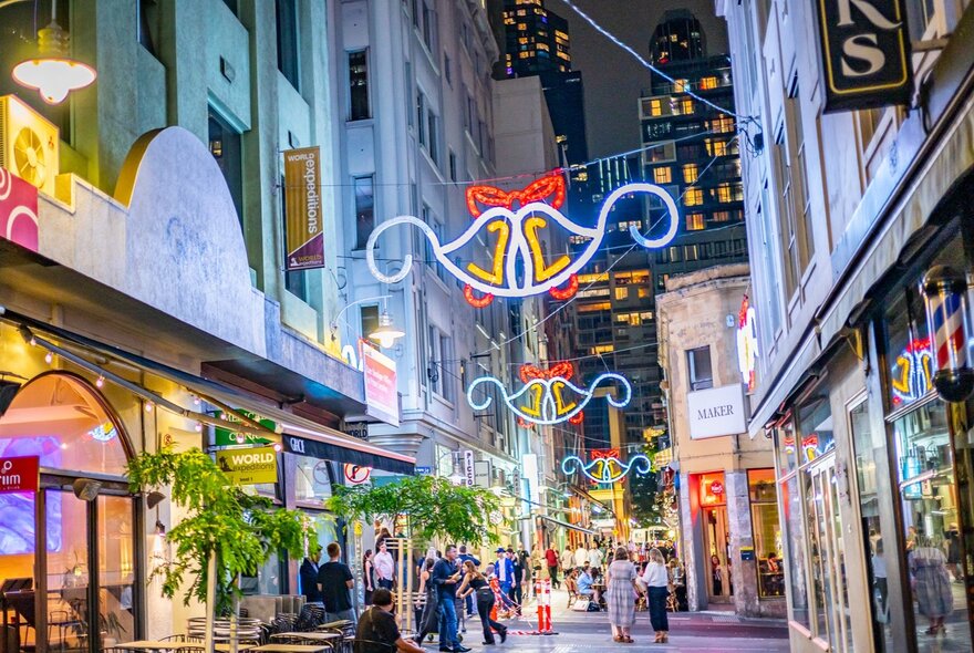 Light up Christmas bell decorations over a laneway full of people. 