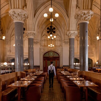 Interior view of the grand and spacious La Reine restaurant showing banquette seating, large marble columns and vaulted ceilings.