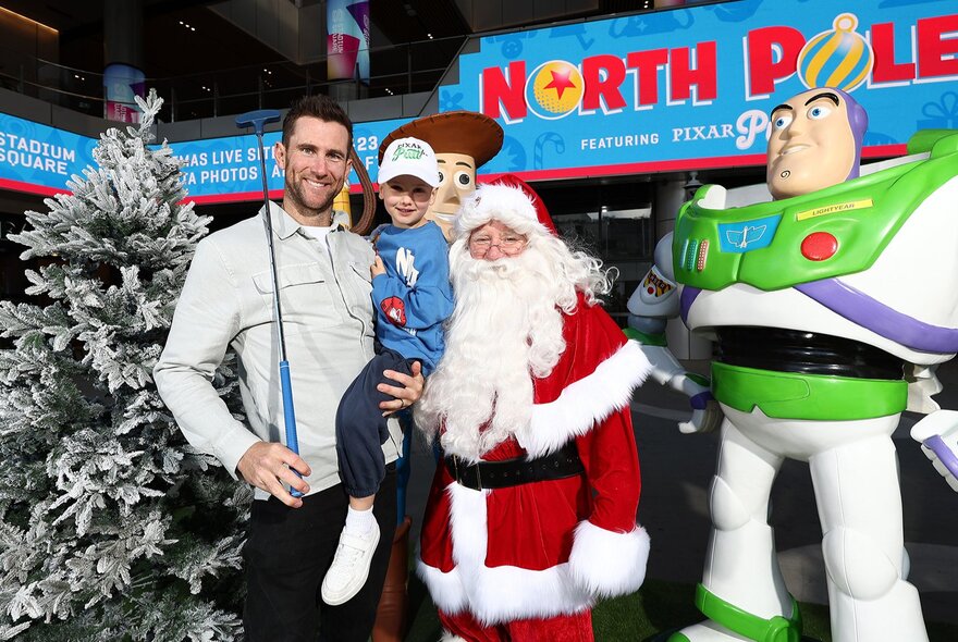 Man and child holding golf club standing next to Santa and Toy Story character.