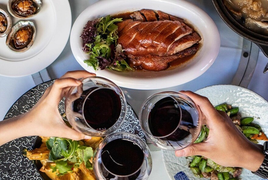 Three glasses held up in cheers over several dishes of food.