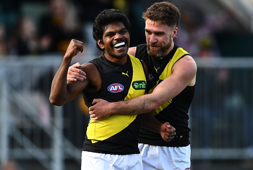Two Richmond football club players embrace and look happy on the field. 