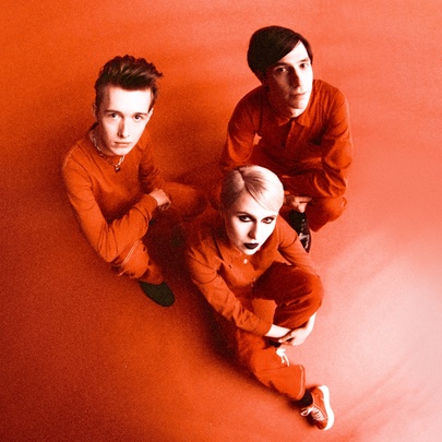 The three members of the alt rock band Papercity wearing red and sitting on a red surface looking up.