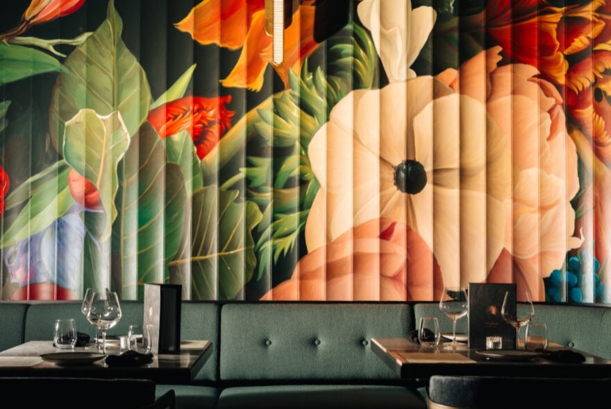 Large, dramatic floral wall mural at Amphora with deep coloured banquettes and small tables. 