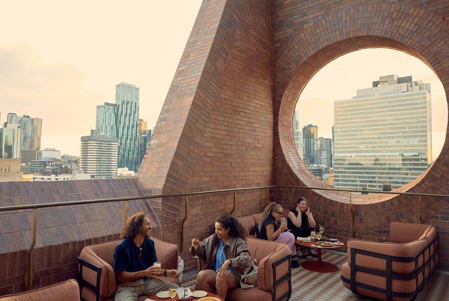 People sitting on couches on a  rooftop bar with cutaway brick walls.