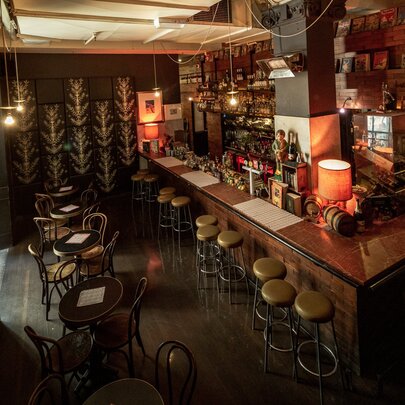Interior of Cookie showing bar area with stools, soft lighting from lamps, and small round tables set for two.