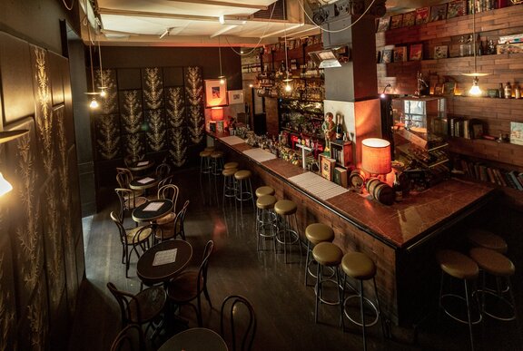 Interior of Cookie showing bar area with stools, soft lighting from lamps, and small round tables set for two.