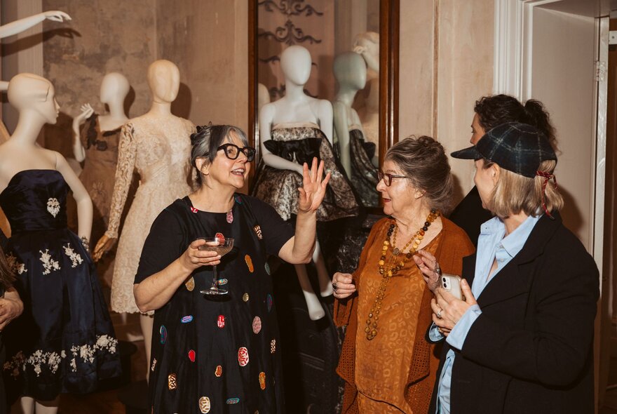 Three people having a conversation in front of three clothing mannequins, in an exhibition room.