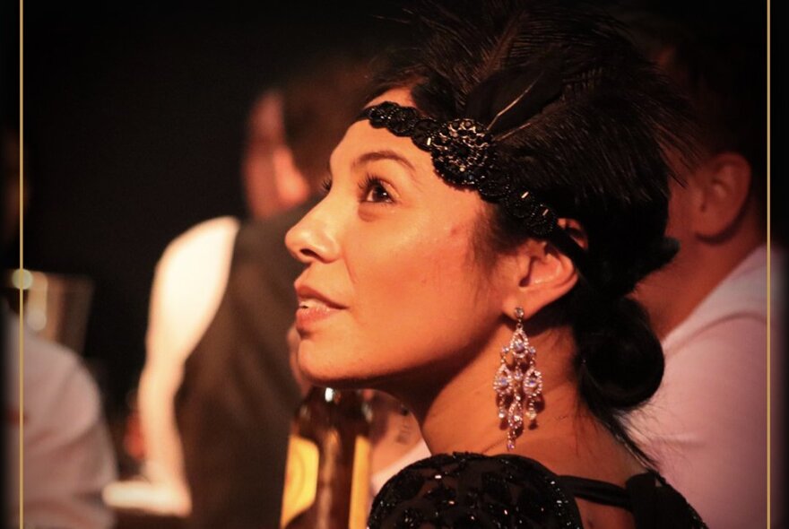 A woman dressed in Art Deco style with a black lace and feathered headband and drop earrings.