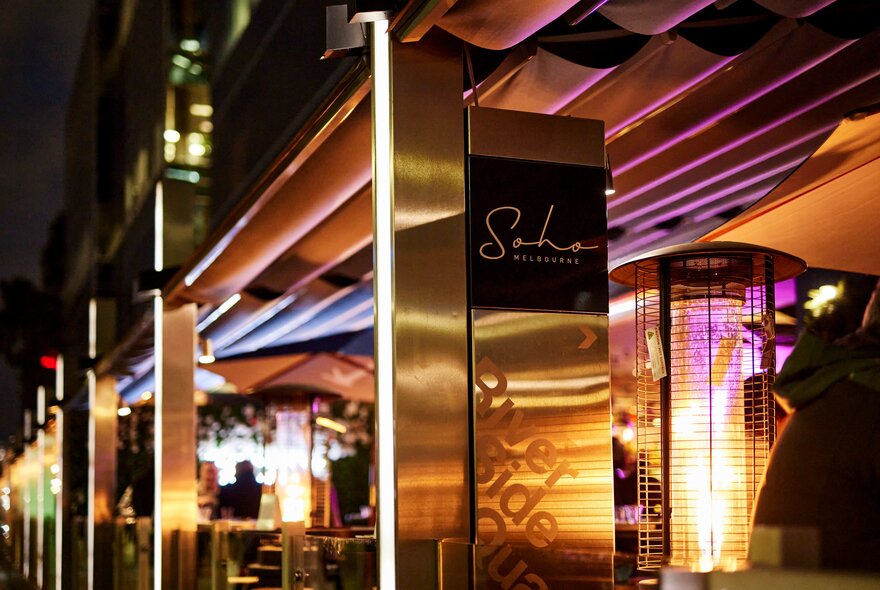 Exterior of Soho Restaurant and Bar at night, showing signage and the waterfront deck area, warmed by large portable heaters.