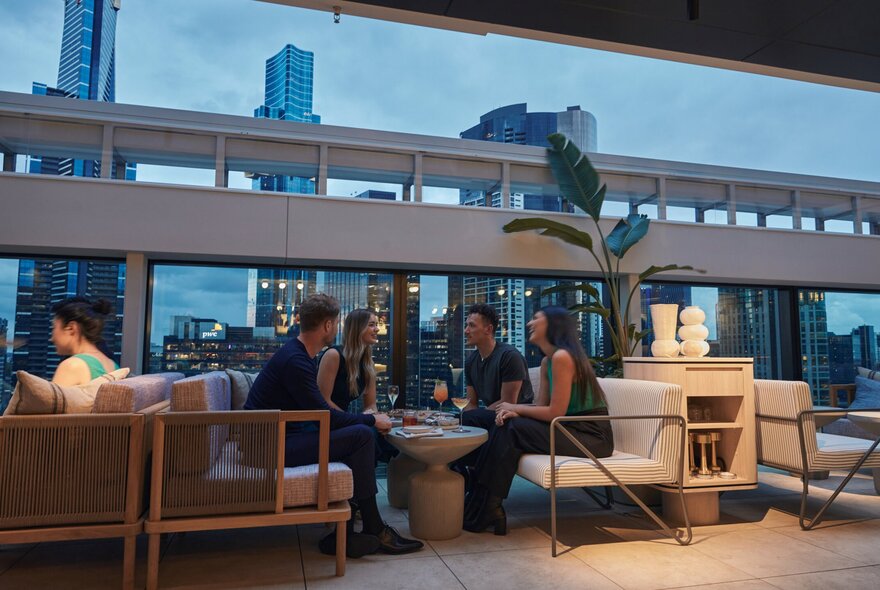 People enjoying cocktails at a rooftop bar with Melbourne's city skyline behind them.