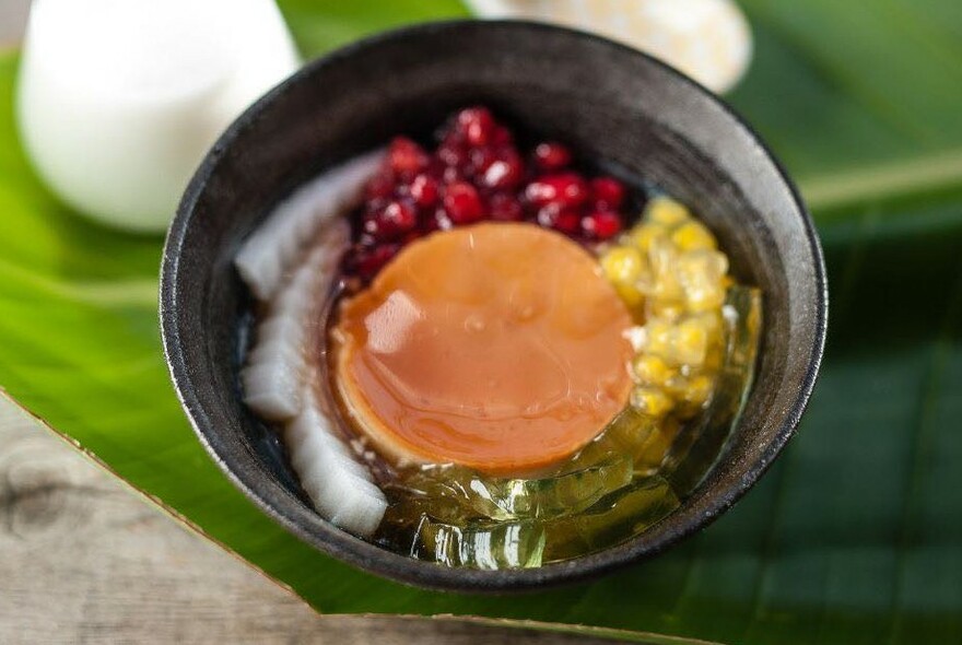 Grey bowl filled with red, yellow, green and white fillings surrounding a light orange circlular jelly.