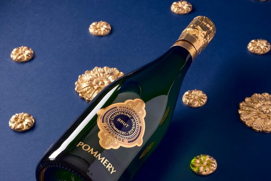 Bottle of Champagne lying on a dark blue background with gold medallions.