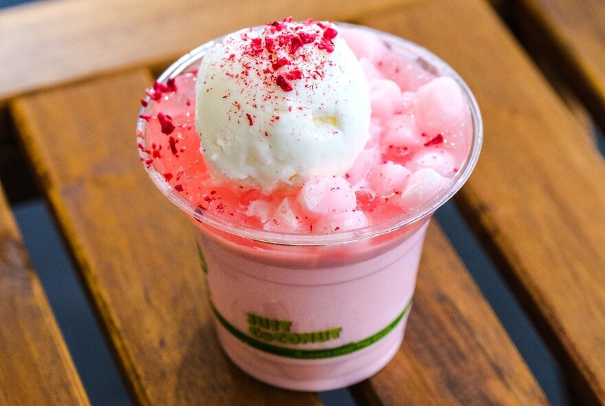 Pink coloured iced coconut drink with ice cream on top.