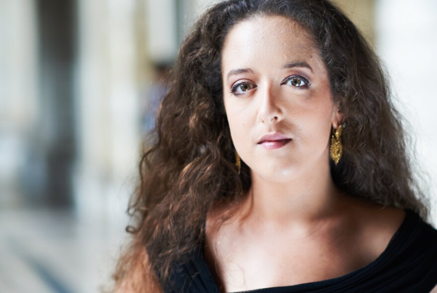 Woman with long curly dark hair, wearing a black outfit.