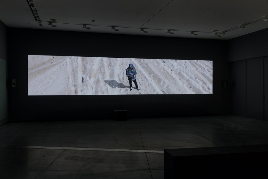 A digital projection of a photo of a person standing in the snow, displayed in a darkened gallery.