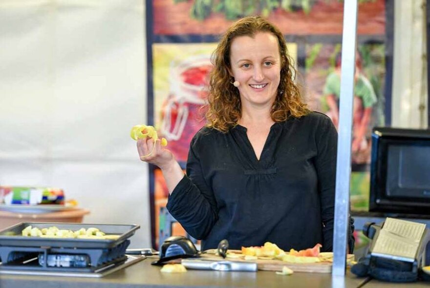 Food presenter holding chopped fruit in a live food presentation setting.