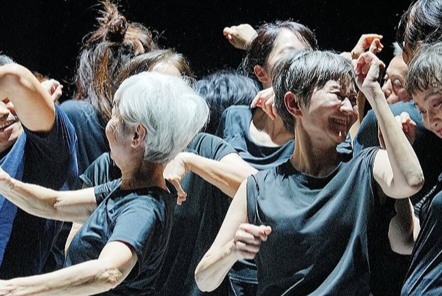 Older people wearing black shirts, dancing in a group.