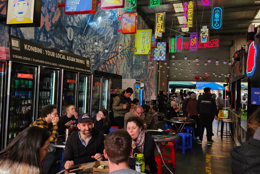 Interior of EziStreat showing people seated at tables in a large warehouse space eating food, colourful signs and bunting overhead.