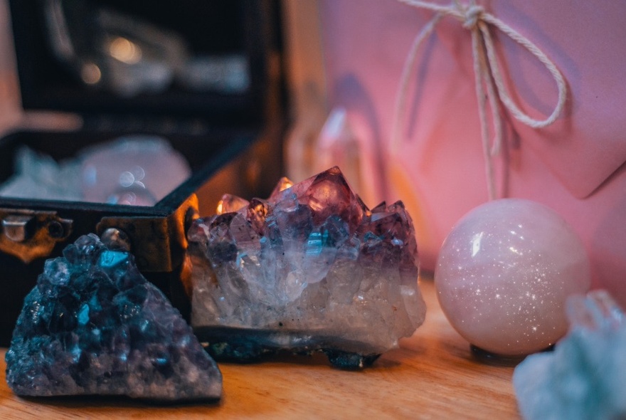 Crystals on a wooden surface in front of large pink envelope and black box.