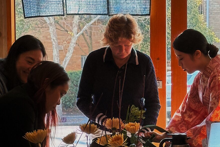 A group of people participating in a traditional Japanese flower arranging Ikebana workshop. 