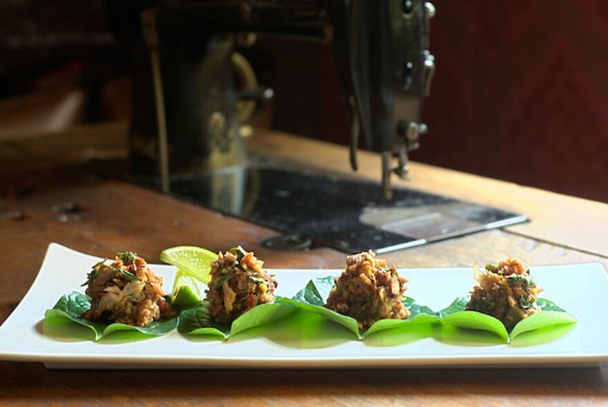 Four small balls of food served on little green leaves.