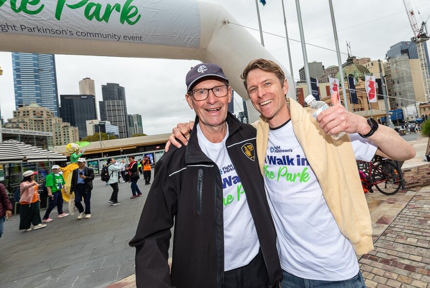 Two men with their arms around each other's shoulders, in front of an inflatable finish line marker.