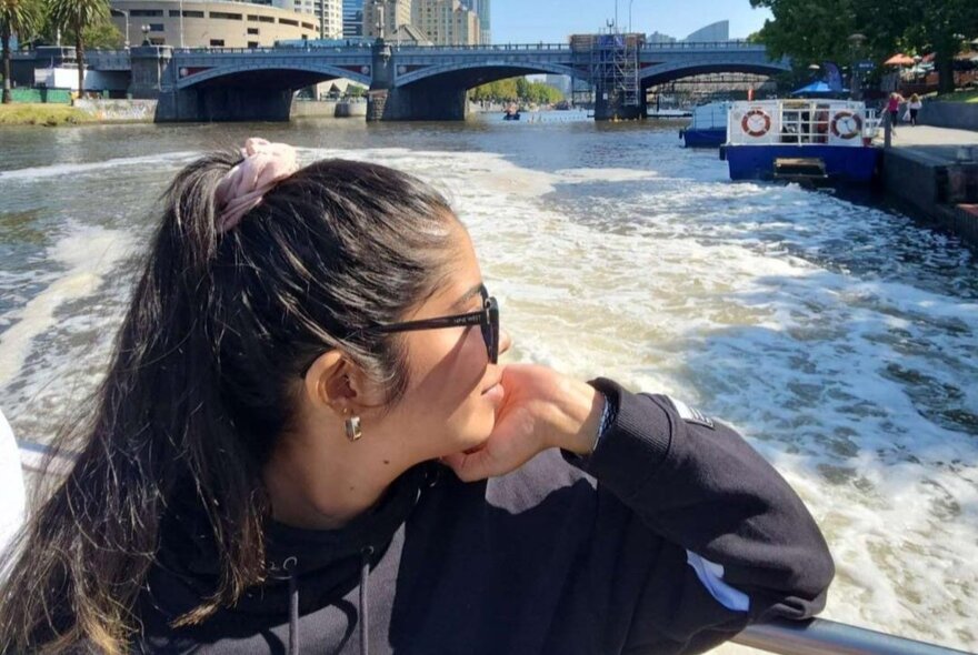 A woman leaning her elbow on the edge of a boat and looking at the view of the Melbourne skyline and Yarra river behind her.