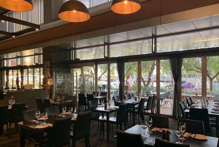 Large restaurant space with many small tables and wine glasses on them.