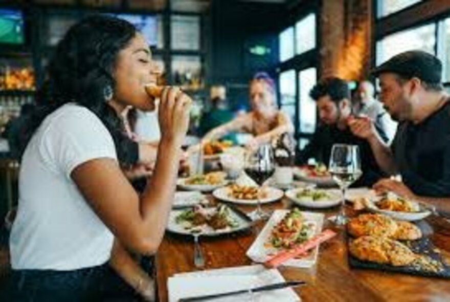 People seated around a table in a restaurant eating food from a range of dishes.