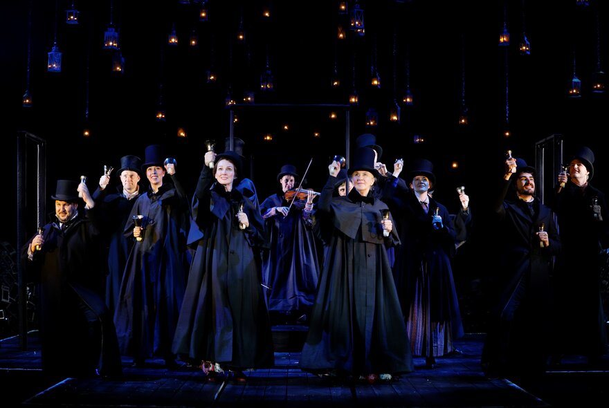 Performers in period dress singing in a row on a dark stage.