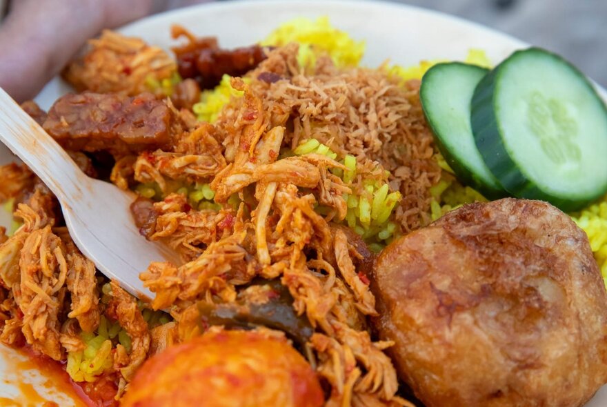 A plate of rice, meat and veggies with a cucumber garnish. 