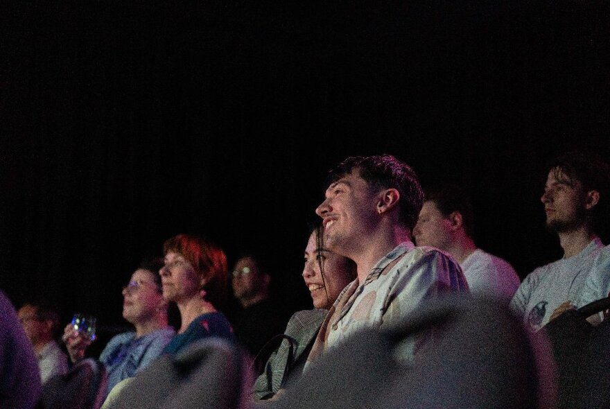 A smiling audience looking up at something on stage.