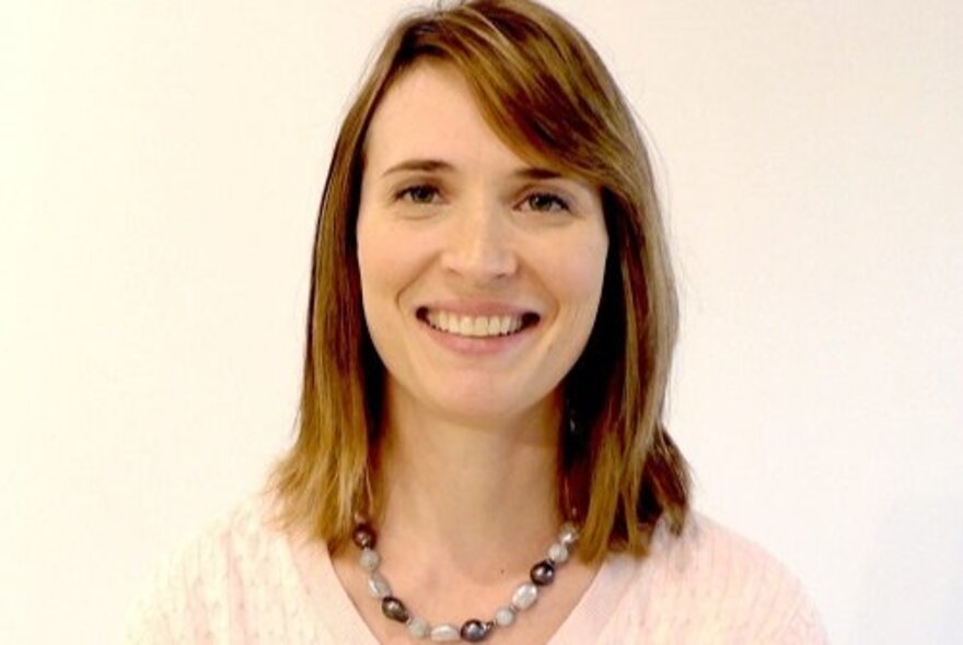 A smiling woman with shoulder-length hair and a beaded necklace. 