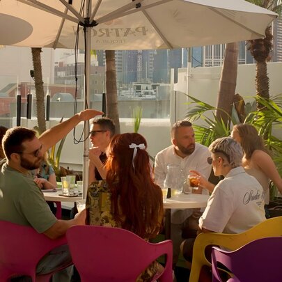 People enjoying drinks and socialising at the rooftop bar at The Carlton Club, with city buildings in the distance.