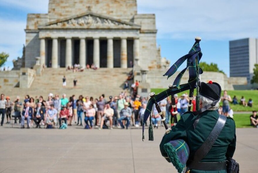 Bagpiper playing in front of people gathered in front of the Shrine of Remembrance steps.
