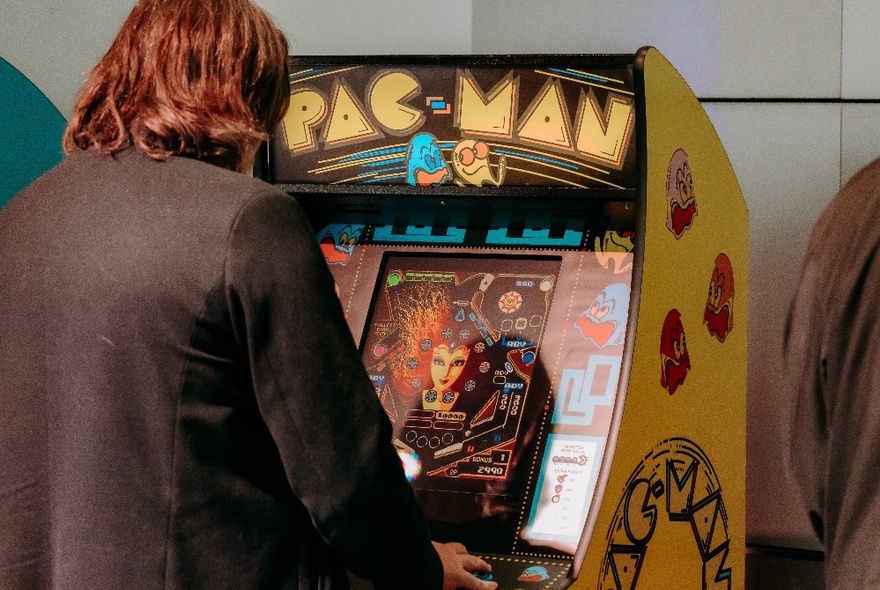 The back of a person playing a Pac Man arcade game. 