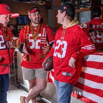 NFL fans wearing red sports outfits including oversized red hat, in a bar setting with striped bar decor.
