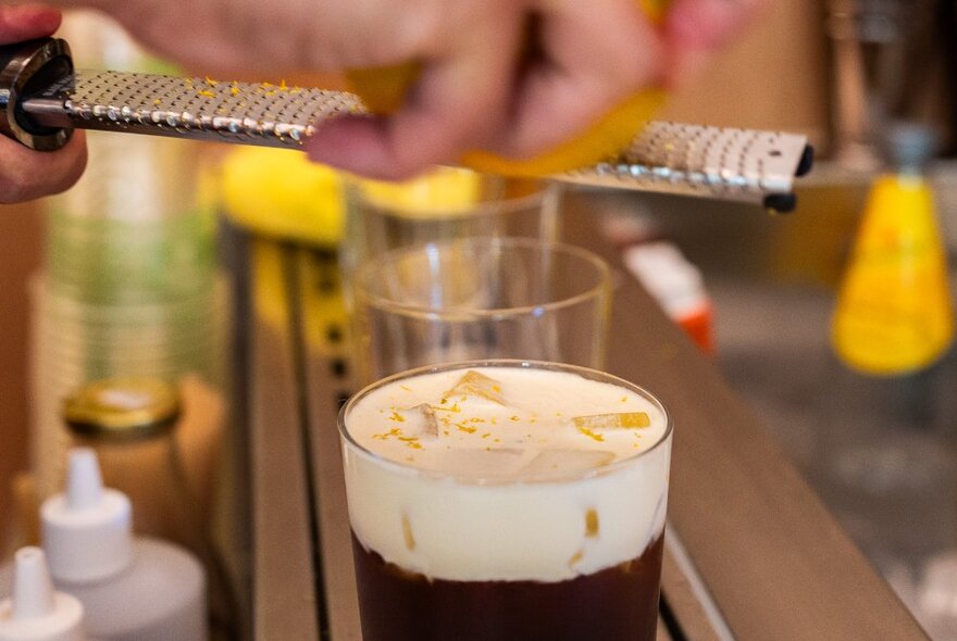 Someone grating citrus with a microplane over a frothy drink.