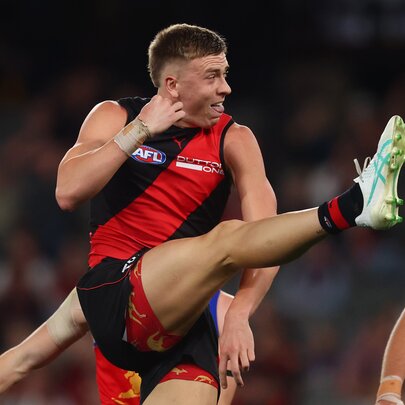 An Essendon AFL football player with his leg raised high in the air, having just kicked the football