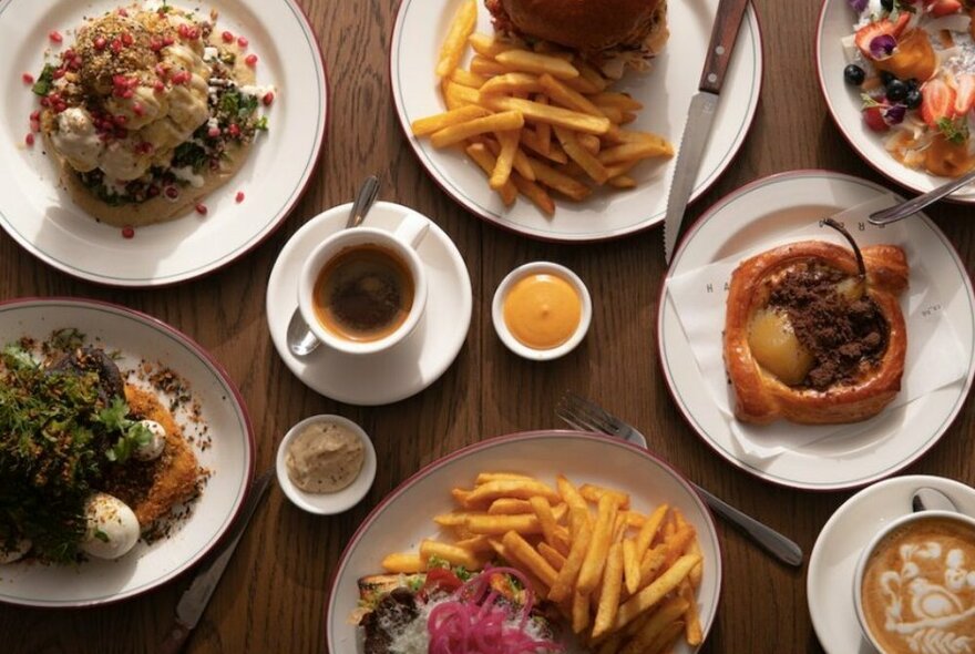 A table of coffees and brunch dishes including pastries, chips, burgers and pancakes.