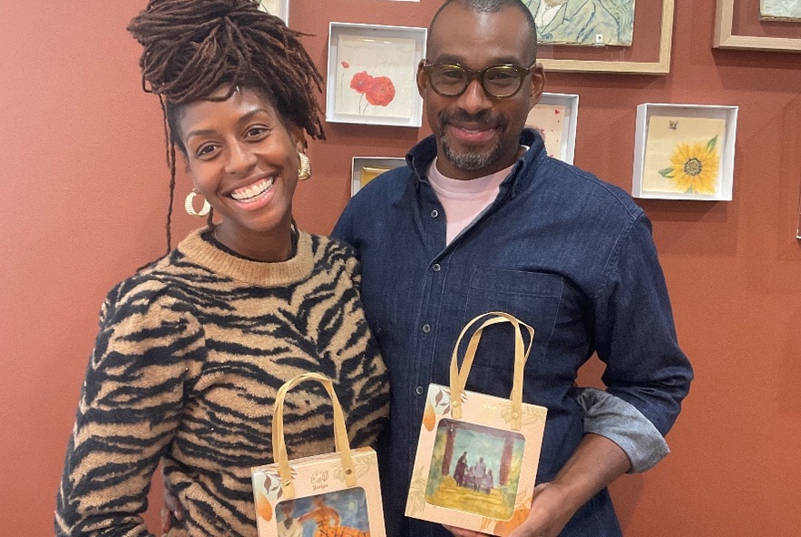 A couple smiling broadly holding up painted chocolates with handles