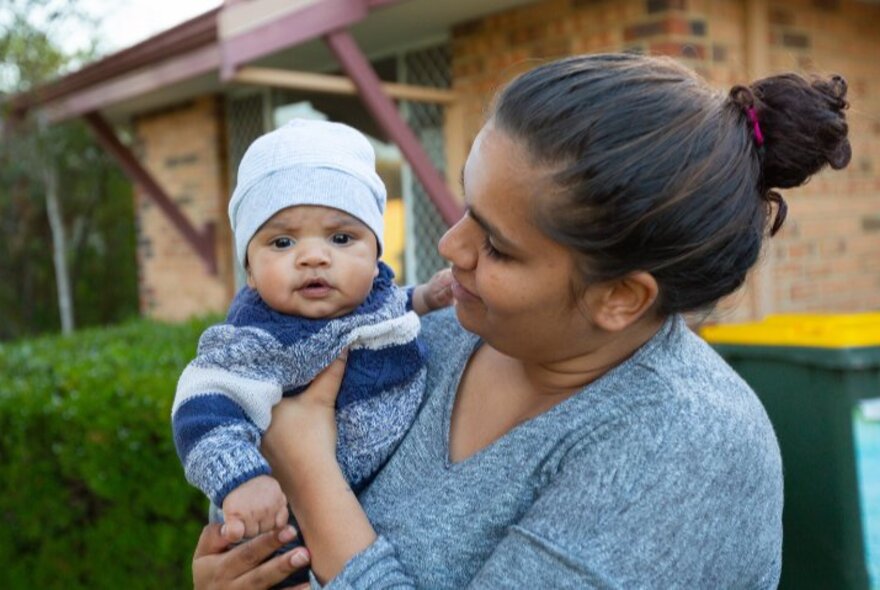 A First Nationals woman holding a baby with a warm jumper and beanie on it's head. 