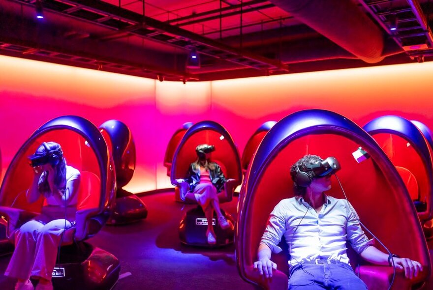 People seated in egg chairs wearing VR headsets.