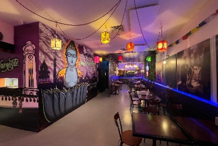 An empty cafe with several tables, a mural and dim coloured lights. 