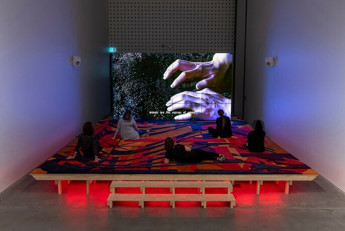 People watching a show on a screen whilst lounging on an artistic and illuminated raised floor.