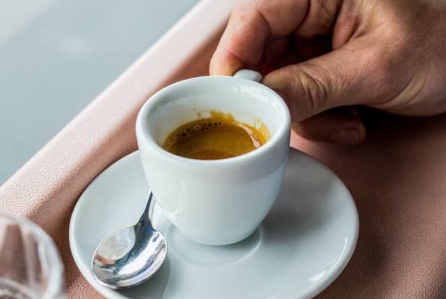 Person holding a small cup of coffee.