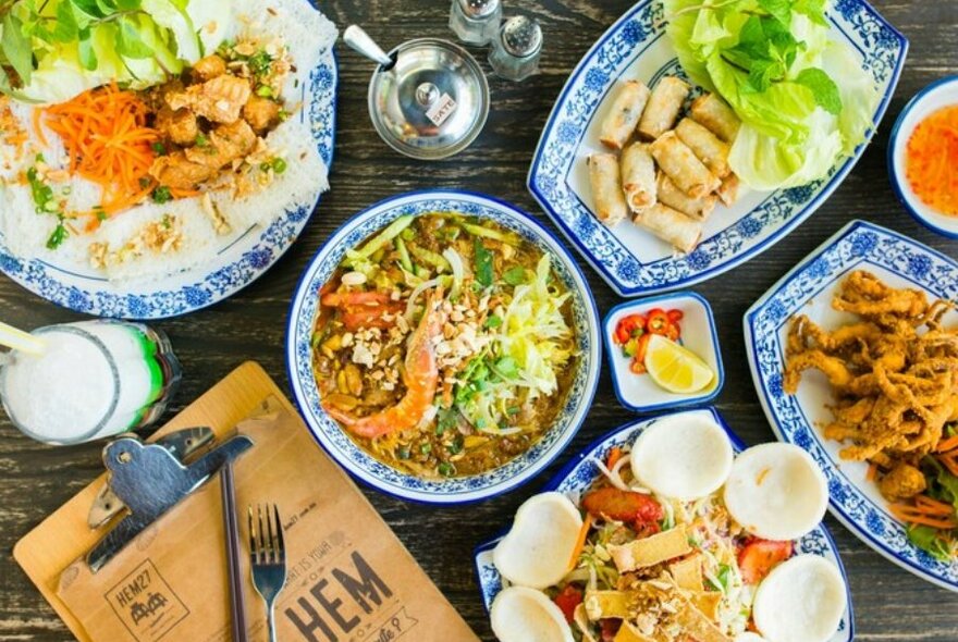 A restaurant table set with Vietnamese dishes including pho, spring rolls, chicken, a stir fry and salt and pepper squid. 