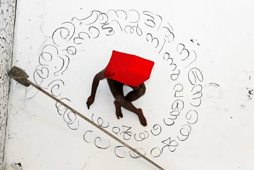 A seemingly naked person seen from above, sitting within a circular representation of Islamic text.