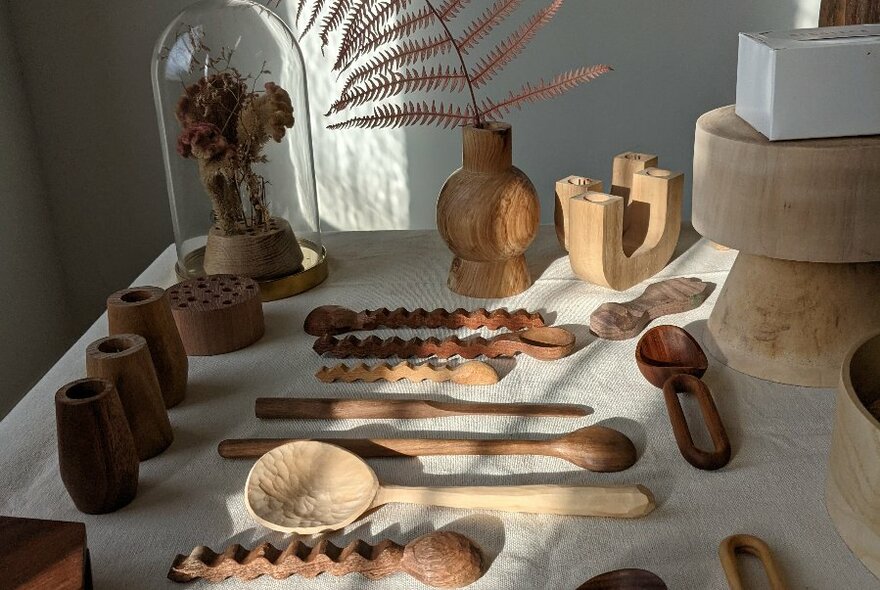 A selection of carved timber spoons, ladles and other objects on a white table.